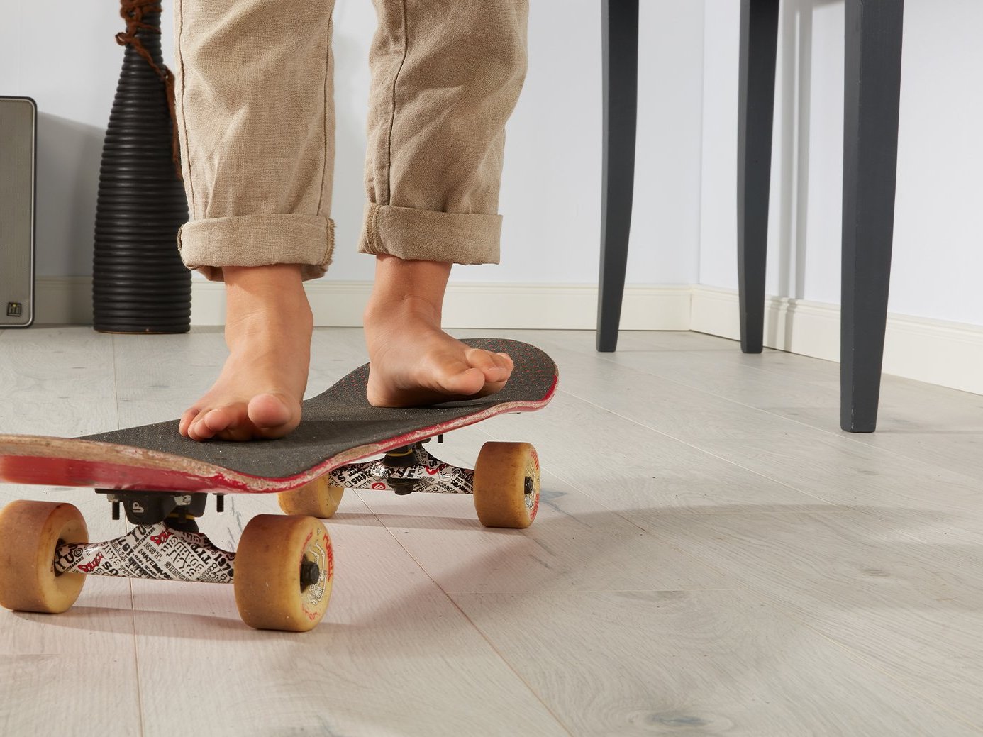 Die Beine eines Jungen, der auf einem Skateboard in der Wohnung steht